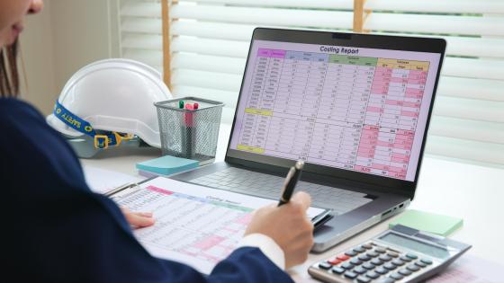 woman working on costs spreadsheet with safety hat on desk