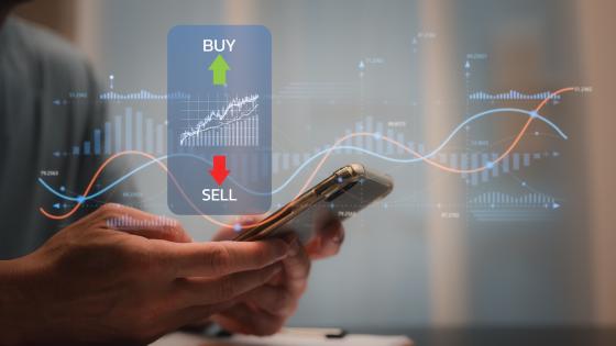 Person using mobile phone with market data in background