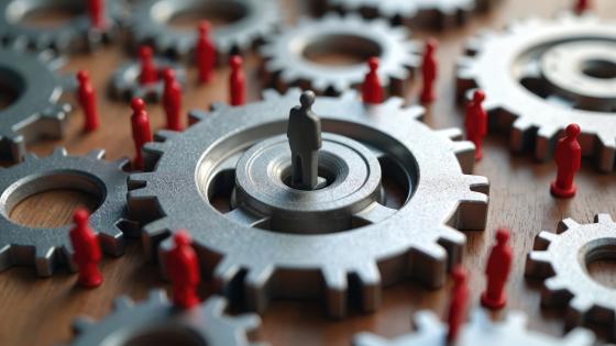 Interconnected gears with red figures and one larger grey figure above