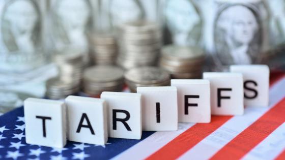  Tariffs" wooden word on US flag with US dollar bills
