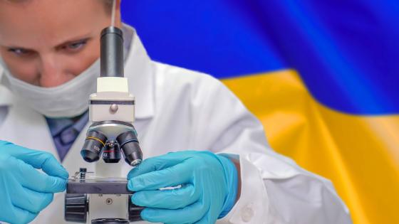 Scientist looking through microscope in front of Ukrainian flag