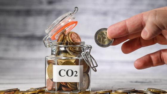 Person putting coins into a jar labeled CO2