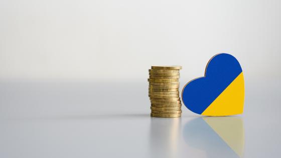 A stack of coins and the flag of Ukraine in the shape of a heart.