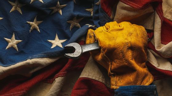 Worn work glove holding wrench tool and gripping old US American flag