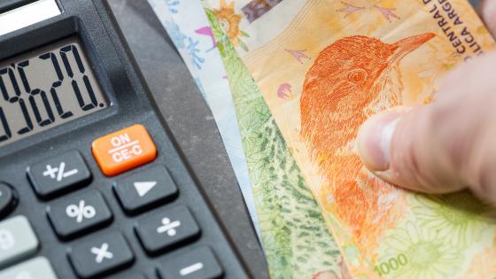 Calculator and hand holding Argentine pesos