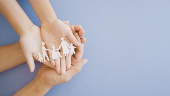 hands holding paper cut outs of multi-generational family
