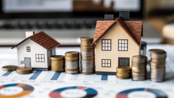 Model houses next to piles of coins and financial charts