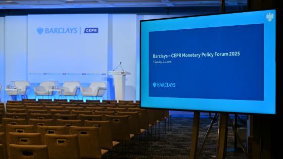 Empty conference room with rows of chairs facing a stage set up for the Barclays–CEPR Monetary Policy Forum 2025. A large screen in the foreground displays the event title and date: Tuesday, 24 June.